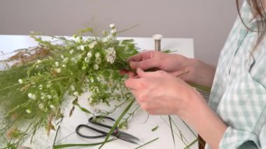 Ivan Kupala şöleni için çiçek dokuma konusunda usta bir sınıf. Kadın taze otlar ve çiçeklerden çelenk dokuyor, pagan sembolü, gündönümü günü. Kırsal stil. Papatya ve bitki çelengi, yaz tatili.