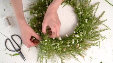 Ivan Kupala şöleni için çiçek dokuma konusunda usta bir sınıf. Kadın taze otlar ve çiçeklerden çelenk dokuyor, pagan sembolü, gündönümü günü. Kırsal stil. Papatya ve bitki çelengi, yaz tatili.