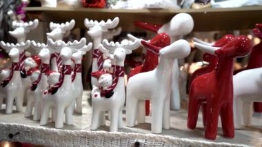 Kışın Noel pazarında seramik beyaz ve kırmızı geyik heykelcikleri, markette hediyeler ve hediyelik eşyalar. Noel ve Yeni Yıl Fuarı 'nda hediyeler ve hediyelik eşyalar, yakın plan dekorasyon.