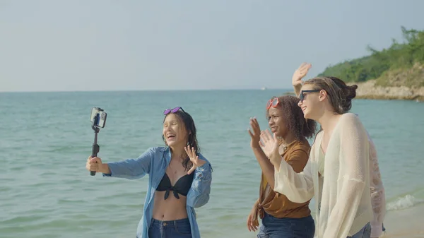 stock image A group of young women using mobile phones to take selfies at the beach on their summer vacation and they smile and enjoy their vacation.