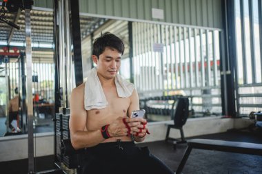 Genç erkek telefon çalıyor ve spor sonrası çeşitli spor ekipmanlarıyla müzik dinliyor..