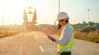 Engineer talking on walkie-talkie and using smart phone for working at construction site