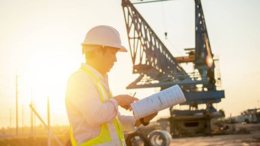 Men Engineer talking on walkie-talkie and holding blueprint for inspecting and working at construction site