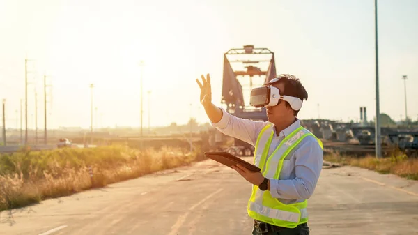 Asian engineer using virtual reality headset and tablet for inspecting and working at construction site