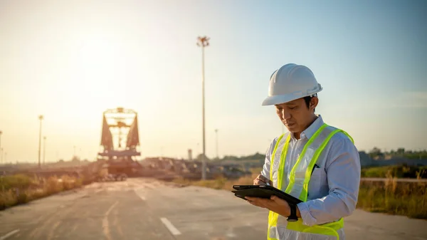 stock image Asian engineer with hardhat using tablet pc computer inspecting and working at construction site