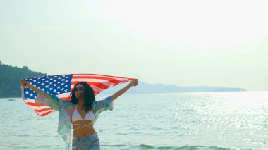 Genç kadınlar yaz tatillerinde kumsalda ve denizde Amerikan bayrakları taşıyorlar ve gülümsüyor ve tatillerinin tadını çıkarıyorlar..