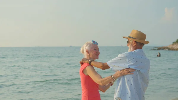 stock image Two elderly men and women dancing at the beach on their summer vacation and they smile and enjoy their day off.