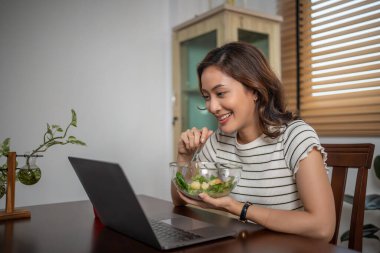 Kadın sağlıklı salata yiyor ve evde çalışıyor.