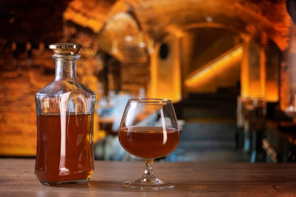 Cognac bottle and glass on the table of old European castle restaurant background - close-up product photo