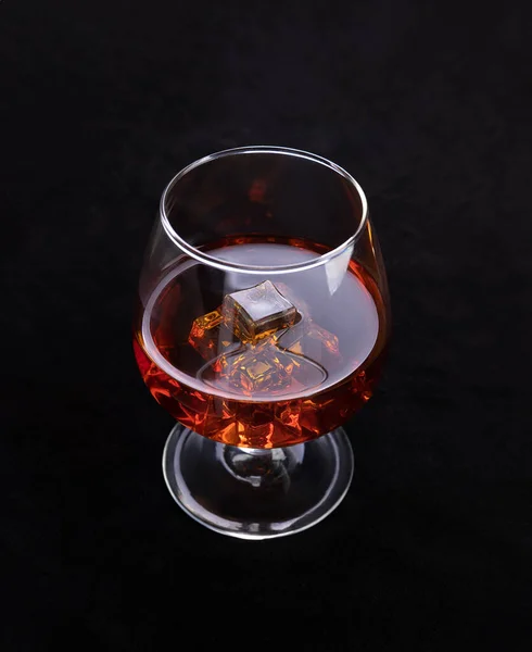 Cognac glass with ice cubes on the table with a luxury leather black background - close-up product photo