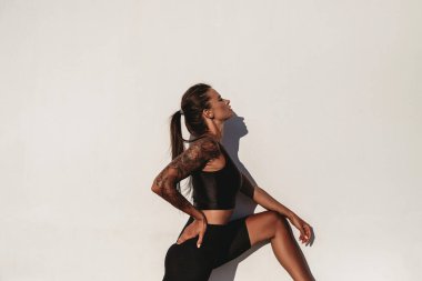 Yazın güneşli bir günde beyaz duvar arkasında bronzlaşmış, bronzlaşmış, beyaz dövmeli bir kadın.