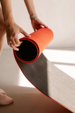 Beyaz tenli genç bir kadının yoga minderini açarken görüntüsü.