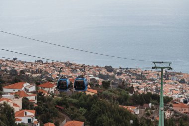 Funchal, Madeira, Portekiz - 24.09.2021: Funchal 'da şehir ve okyanusun üzerinde kulübeleri olan kablo araba