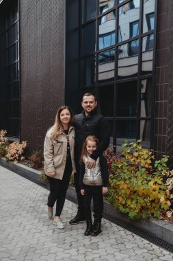 Mutlu aile babası anne ve sevimli küçük kız modern ofis binasının önünde parkta yürüyorlar.