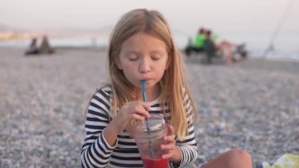 黄昏时 一个小女孩在海边享受着鲜榨的果汁 — 图库视频影像