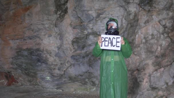一个戴着防毒面具和防护服的女人站在那里 海报上写着一句话 洞穴里的和平 — 图库视频影像