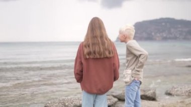 Bir kız ve bir oğlan bulutlu bir sonbahar gününde deniz kenarında yürürler..