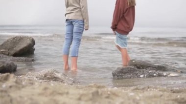 İki gencin çıplak ayakları denizden uzakta duruyor, küçük dalgalar..