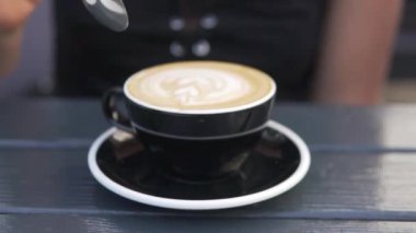 Kişi kaşıkla kahve karıştırıyor. Bir kadın bir kaşık Cappuccino 'yu şık siyah bir fincanda engelliyor..
