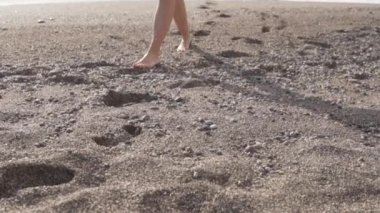 Kadınların ayakları kumlu sahilde yürür..