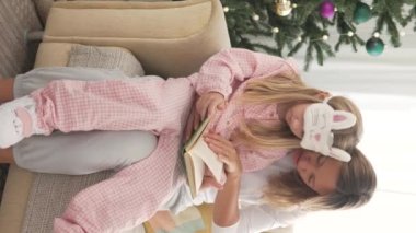 Bir kadın Noel sabahı evde küçük bir kız kitabı okuyor..
