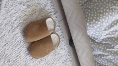 Dikey video, yakın plan. Bir kadın yataktan kalkar, ayaklarını sıcak terliklere sokar..