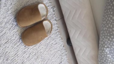 Bir kadın yataktan kalkar ve kürk terliklerini giyer. Dikey video, bacaklara yakın çekim.