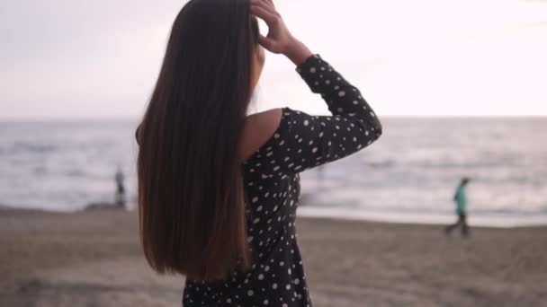 Μια Όμορφη Μελαχρινή Γυναίκα Προσαρμόζει Μακριά Σκούρα Μαλλιά Της Παραλία — Αρχείο Βίντεο