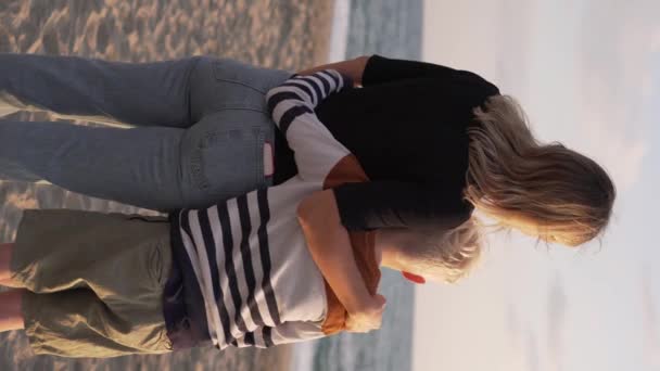 一位母亲抱着金发碧眼的儿子 俯瞰夕阳的大海 垂直录像 一个带着一个男孩在海上度假的女人 — 图库视频影像
