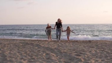 Çocukları, oğlu ve kızı olan mutlu bir kadın kumsalda el ele koşuyor..