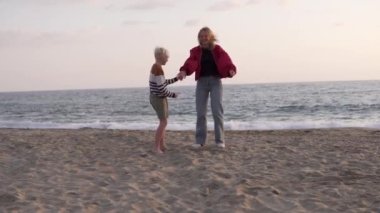 Mutlu anne ve oğul el ele tutuşarak sahilde zıplıyorlar. Türkiye, Alanya, deniz kenarındaki neşeli turistler