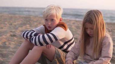 Beautiful children, brother and sister sitting on the beach in the evening at sunset, close-up, sunset light.