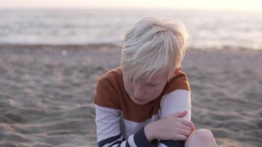 A handsome brooding boy is blonde against the backdrop of the sea.