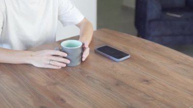 Womens fingers nervously bang on the table and cup of tea waiting for a phone call.