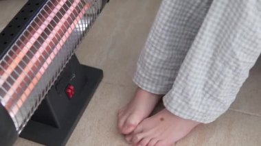 A child warms his feet at an electronic battery at home. Winter in Europe