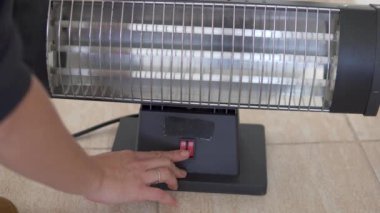 A womans hand turns on the electric heater, the spirals of the heater turn red.