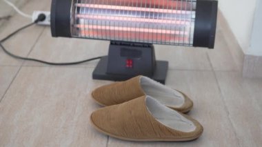 Womens feet wear slippers next to a warm heater on the tiled floor.