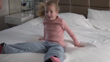 A cheerful little girl falls on the bed in the hotel.