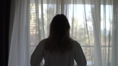 Beyaz önlüklü bir kadın perdeleri açar ve güneşli balkona çıkar. Otel Türkiye, Belek