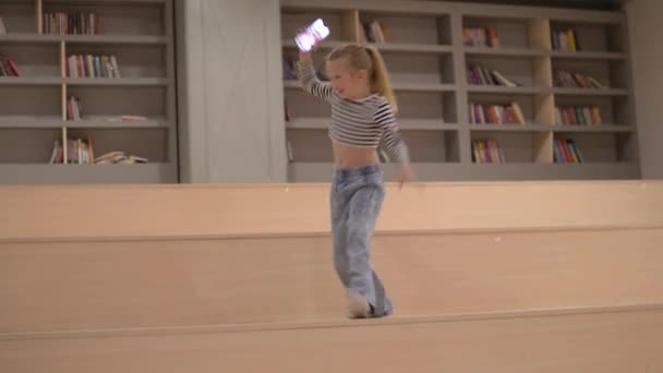 Стильная Маленькая Девочка Телефоном Руках Танцует Библиотеке — стоковое видео