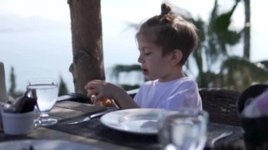 Çocuk deniz kenarındaki terasta bir restoranda yemek yiyor..