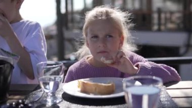 Aç küçük bir kız caddedeki bir restoranda ekmek yiyor..