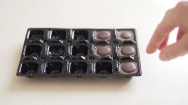 A womans hand takes one chocolate candy out of a box.
