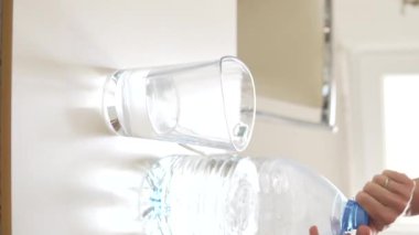 Vertical video, a man without a face pours drinking water from a large bottle into a carafe.