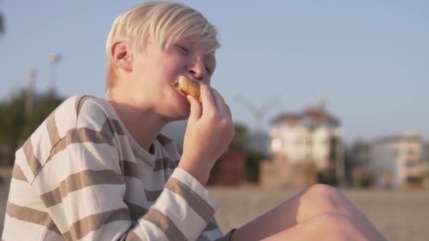空腹の少年は街のビーチでクロワッサンを食べます トルコ Alanya — ストック動画