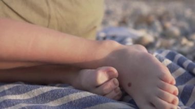 Close-up of a boys feet on a pebble beach, a child on a towel.