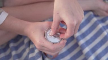 A child opens a drink in an aluminum can on the beach.