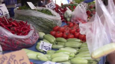 A person picks up zucchini in a bag at a vegetable market.