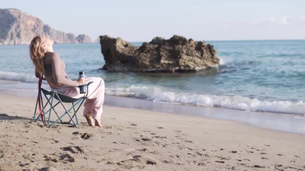 Μια Όμορφη Γυναίκα Κοιτάζει Θάλασσα Μια Τουριστική Καρέκλα Ένα Θερμός — Αρχείο Βίντεο