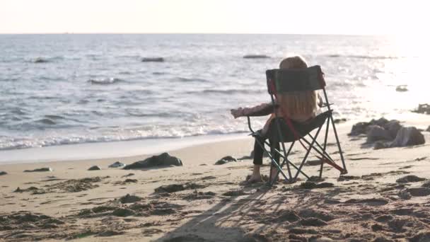 Gün Batımında Küçük Bir Kız Deniz Kenarında Bir Sandalyede Oturur — Stok video